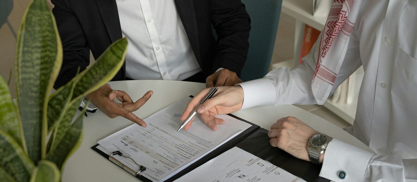 two men sitting at a table with papers and a pen